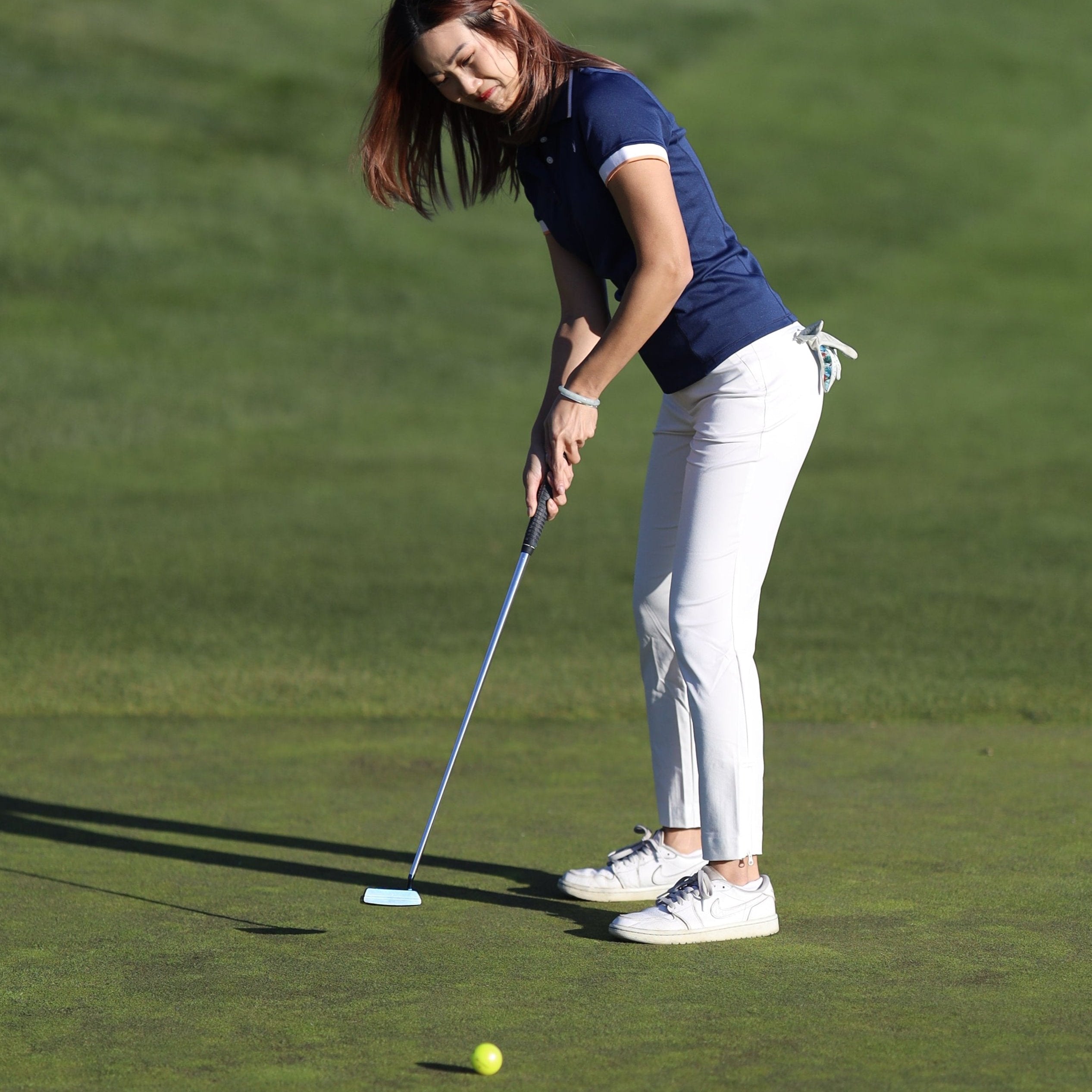 Woman putting on a golf green wearing a navy polo shirt and white golf pants