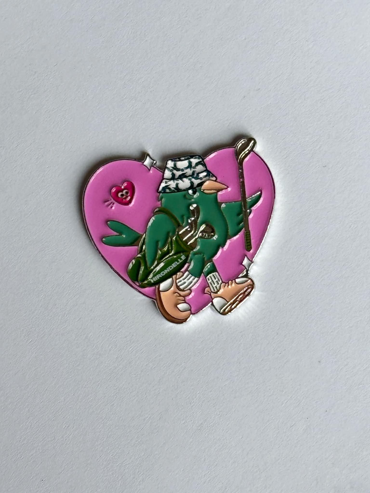 Golf Ball marker with a character in green pants and white hat on a pink heart background named elle from hirondelle 