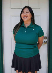 Woman wearing a green polo shirt and black skirt standing in front of a white door.