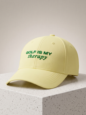 Yellow cap with 'Golf is my therapy' text on a light gray background